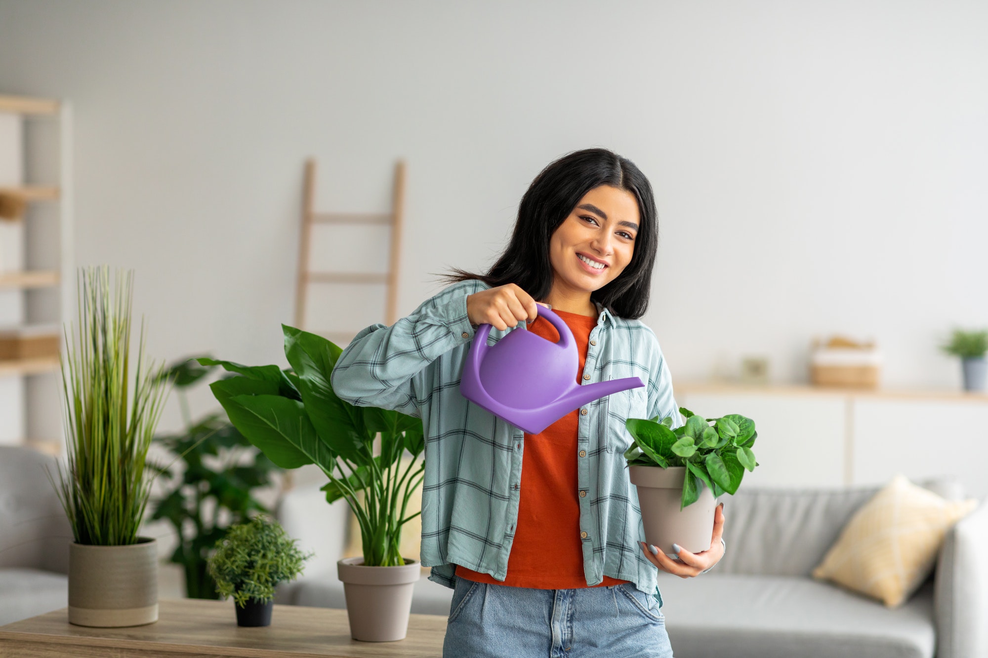 Domestic life. Portrait of beautiful young Arab woman taking care of houseplants, gardening at home